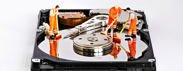 Three tiny people cleaning the inside of a hard drive